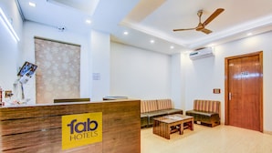 A hotel reception area with a wooden reception desk, a sofa, a coffee table, and a ceiling fan. - Fabhotel Floyd (New Delhi)