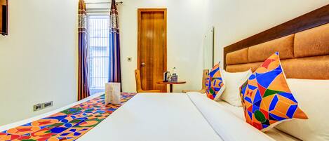 A hotel room with a large bed, a wooden headboard, a small table with a radio, and a colorful carpet.