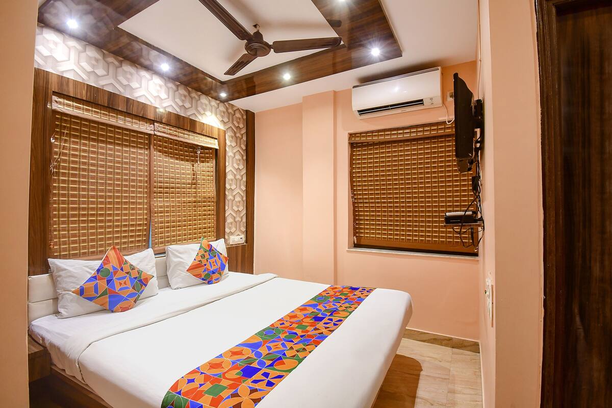 A bedroom with a bed, a ceiling fan, an air conditioning unit, and a TV mounted on the wall.