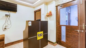 A reception desk with a 'fab hotels' sign, a flat-screen TV mounted on the wall, and a wooden door with a glass panel. - Fabhotel Shree Pushpraj (Kanpur)
