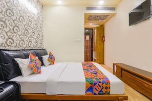 Habitación de hotel con cama, sofá de cuero negro, banco de madera, pared con diseño y televisor montado en la pared.