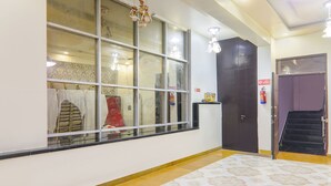 A hallway with patterned flooring, a large window with multiple panes, and a door with a fire extinguisher mounted on the wall. - Fabhotel Shree Pushpraj (Kanpur)