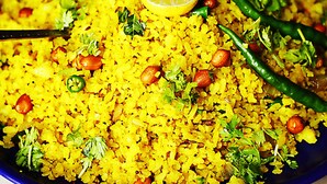 A plate of yellow rice with peanuts, green chilies, and a lemon slice. - Fabhotel Shree Pushpraj (Kanpur)