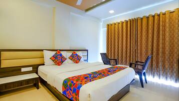 A hotel room with a bed, a bench, a chair, a ceiling fan, and curtains.