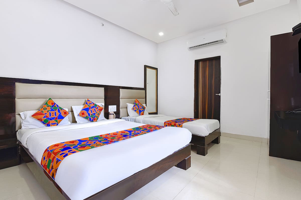 A hotel room with a large bed, two smaller beds, a mirror, an air conditioning unit, and a door.