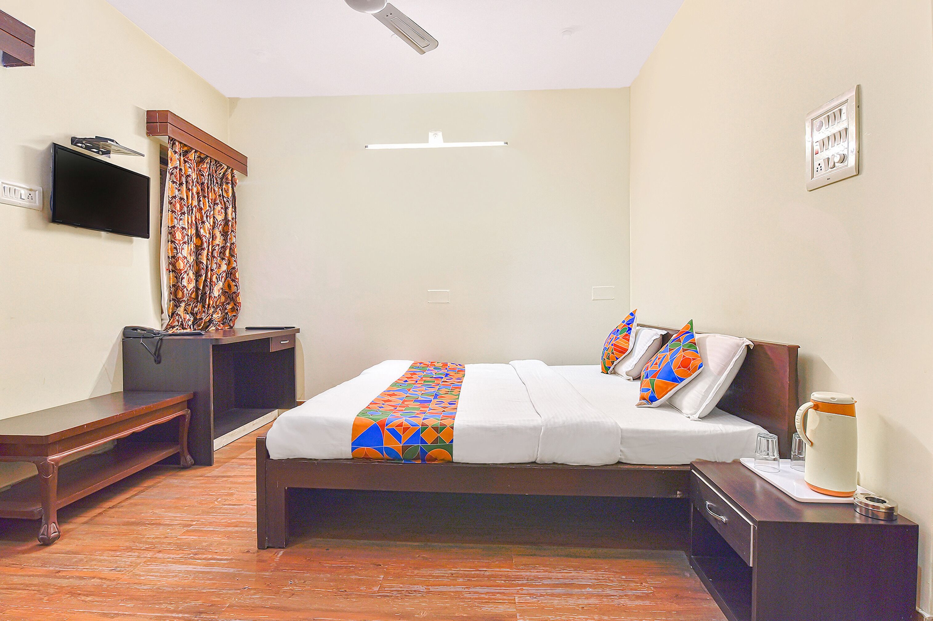 A hotel room with a bed, bedside table, TV, and a power outlet on the wall.