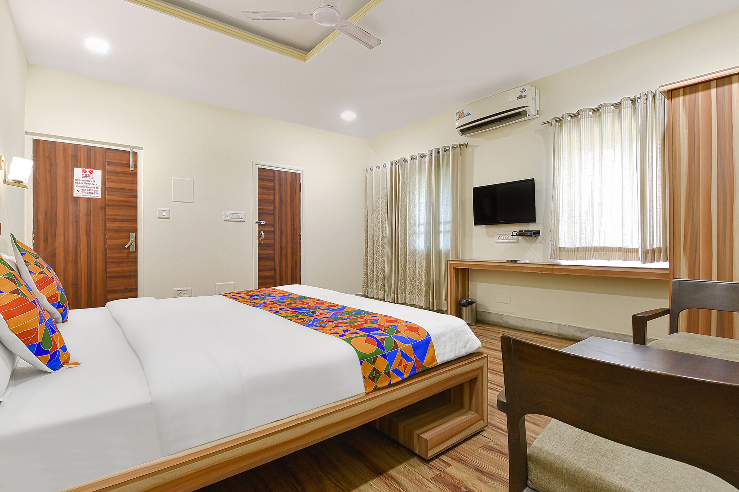 A hotel room with a bed, a desk with a chair, a television, and an air conditioning unit.