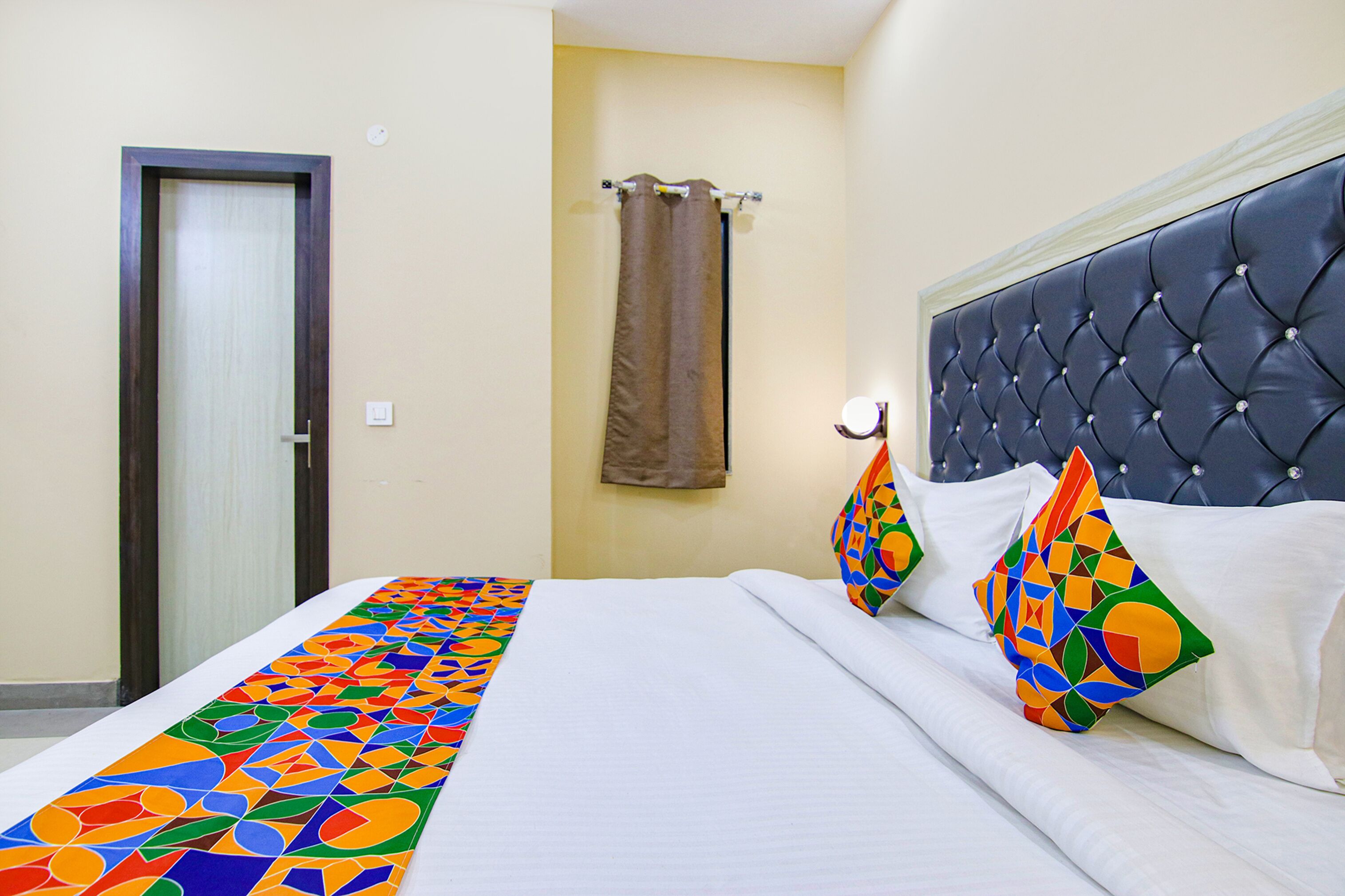 Een hotelkamer met een bed, een hoofdeinde, een gordijn en een deur.