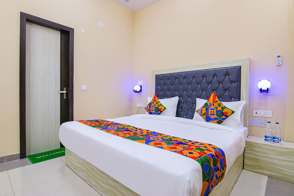 A neatly made bed with a colorful bedspread, a tufted headboard, and two wall-mounted nightstands with water bottles.