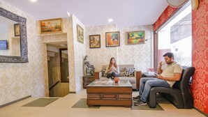 A room with patterned wallpaper, a wooden coffee table, a sofa, and a chair. There are paintings on the wall and a mirror. - Fabhotel Town Pride (Mohali)