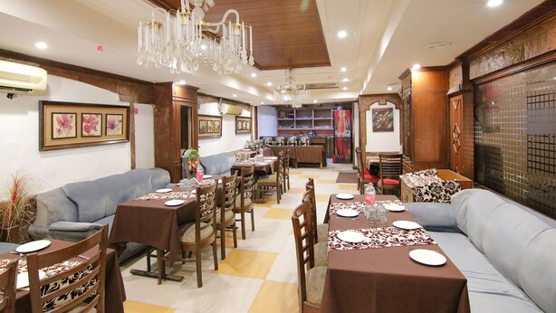 A dining area with tables and chairs, a chandelier, and a sofa. - Fabhotel Town Pride (Mohali)
