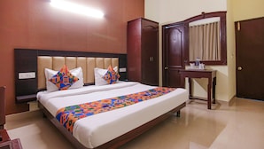 A hotel room with a large bed, a wooden wardrobe, a bedside table with a mirror, and a wall-mounted light. - Fabhotel Town Pride (Mohali)