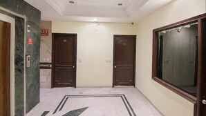 A hallway with marble flooring, two wooden doors, and a large window. - Fabhotel Town Pride (Mohali)