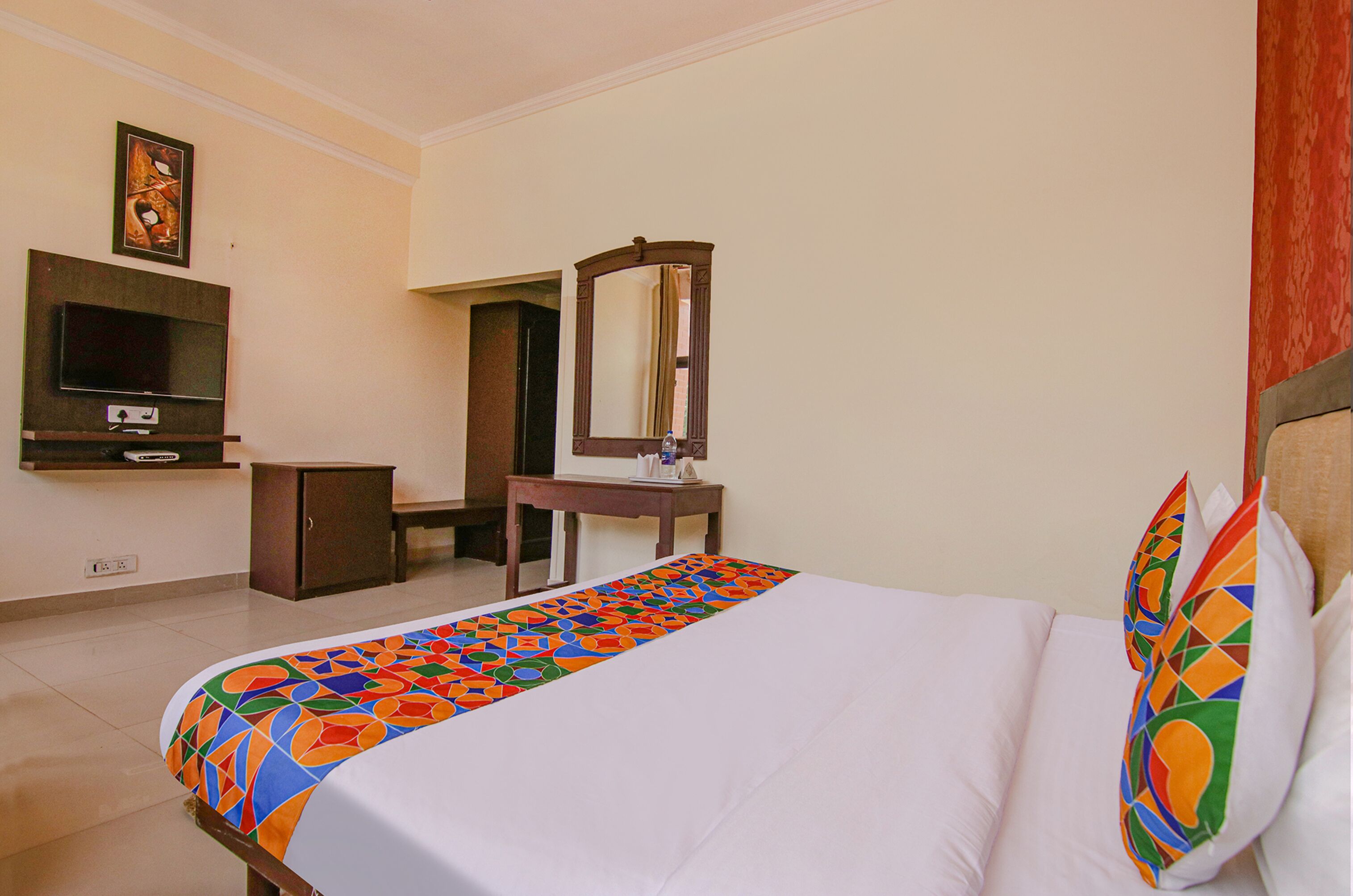 Quarto de hotel com cama, escrivaninha, televisão e espelho.