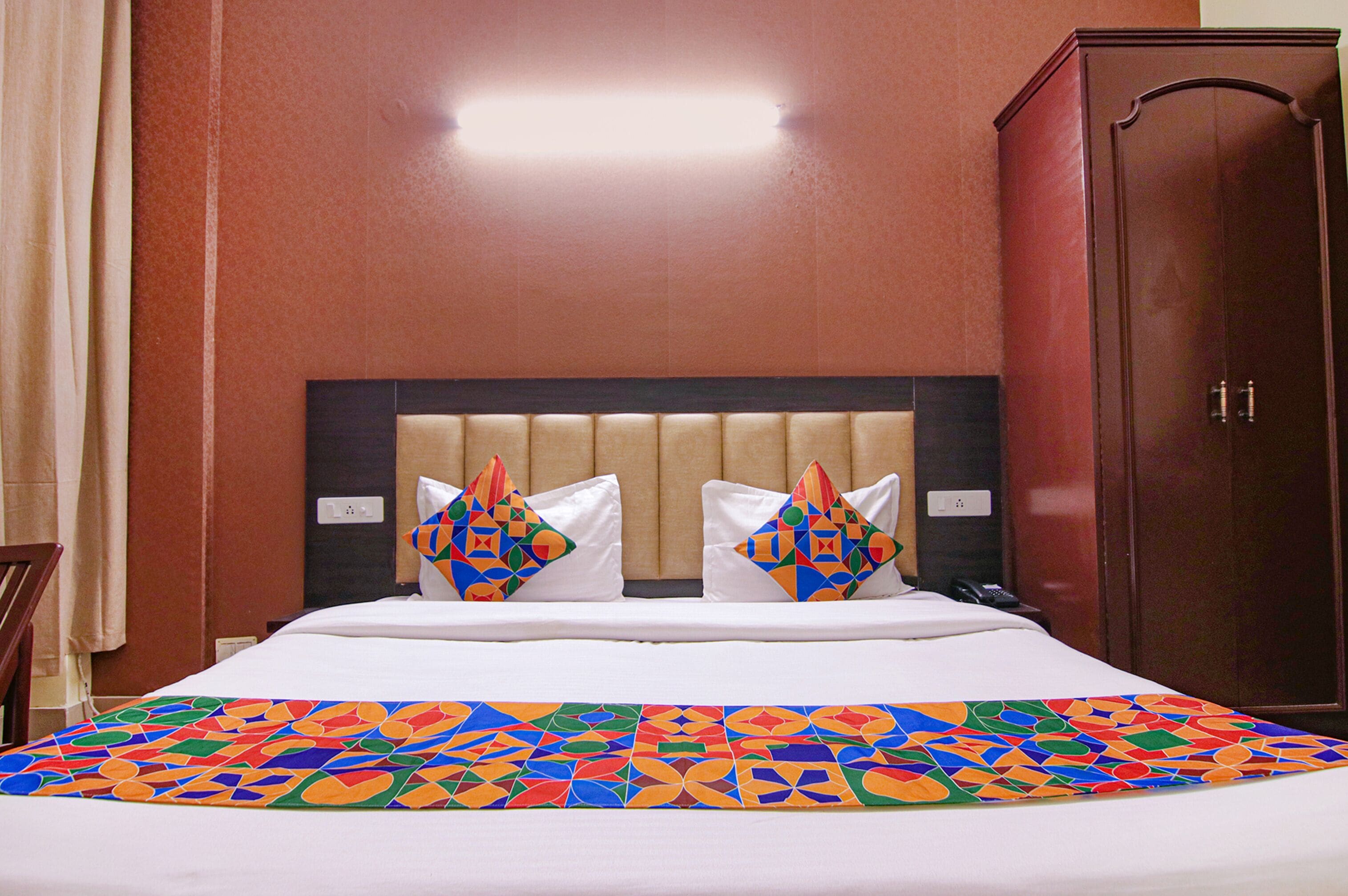 A hotel room with a bed, two decorative pillows, a nightstand, and a wardrobe.