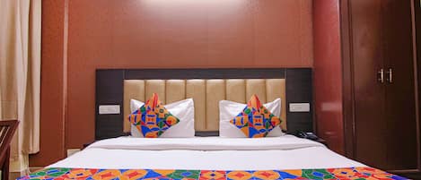 A hotel room with a bed, two decorative pillows, a nightstand, and a wardrobe.