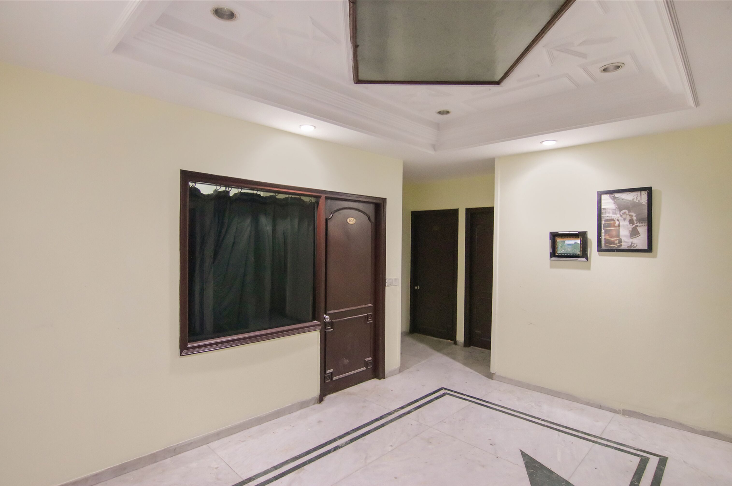 Un corridoio con una porta, un quadro appeso al muro e un pavimento decorato.