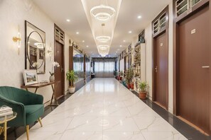 Un vestíbulo de hotel con suelo de mármol, un sillón verde, una recepción y una araña.