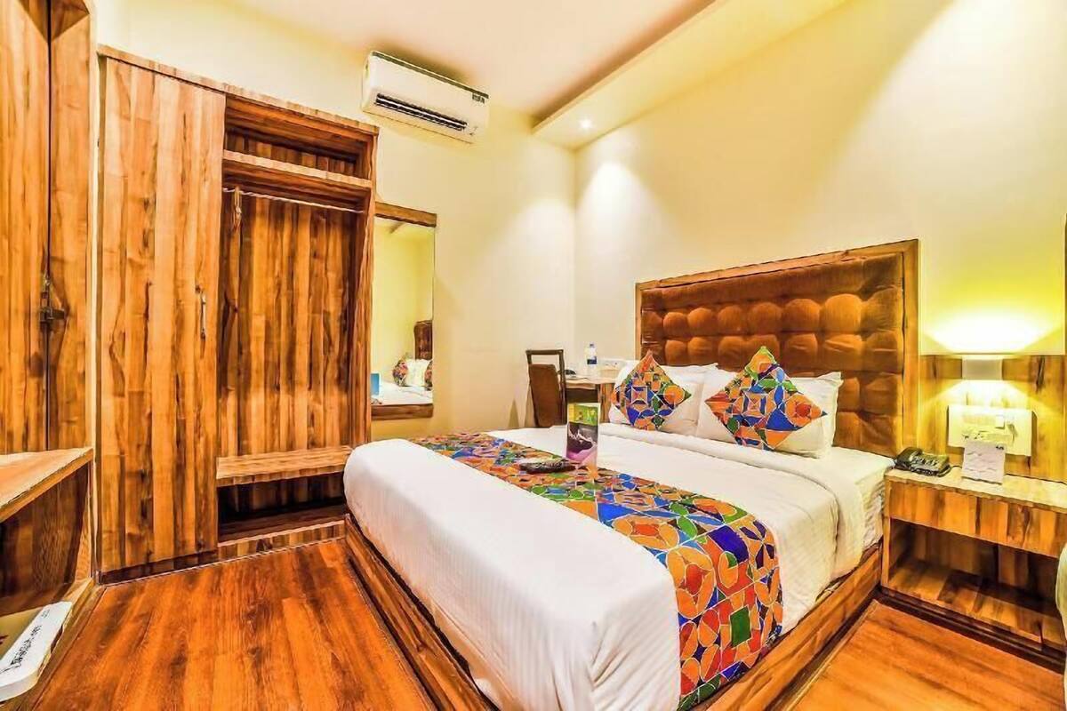 Une chambre d’hôtel avec une armoire en bois, un lit recouvert d’une courtepointe colorée, une table de chevet avec une lampe et un miroir.
