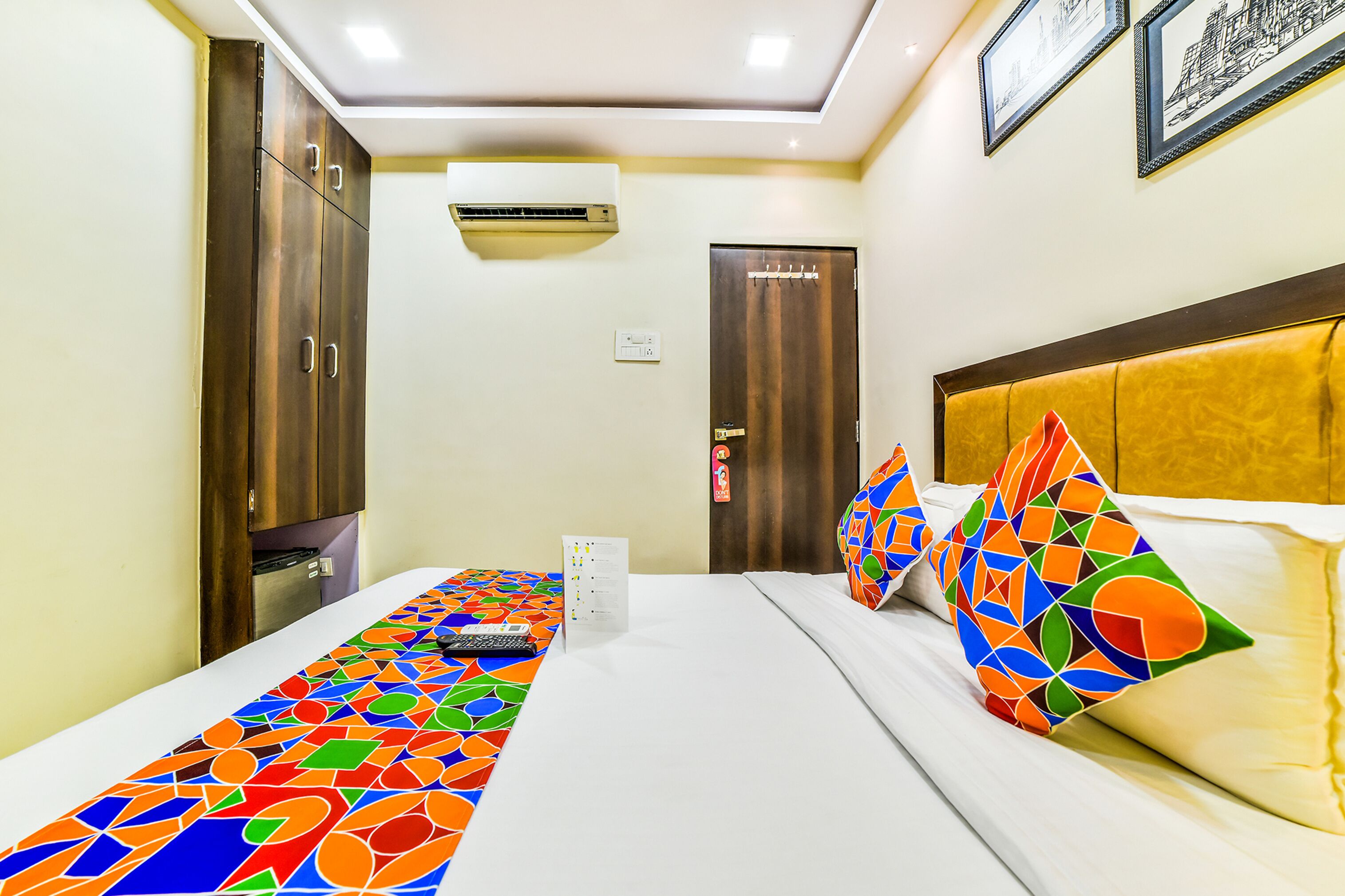 A hotel room with a bed, a desk, a chair, a wardrobe, and an air conditioning unit.