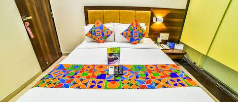 A hotel room with a bed, a nightstand, a framed picture on the wall, and a colorful geometric-patterned bedspread.