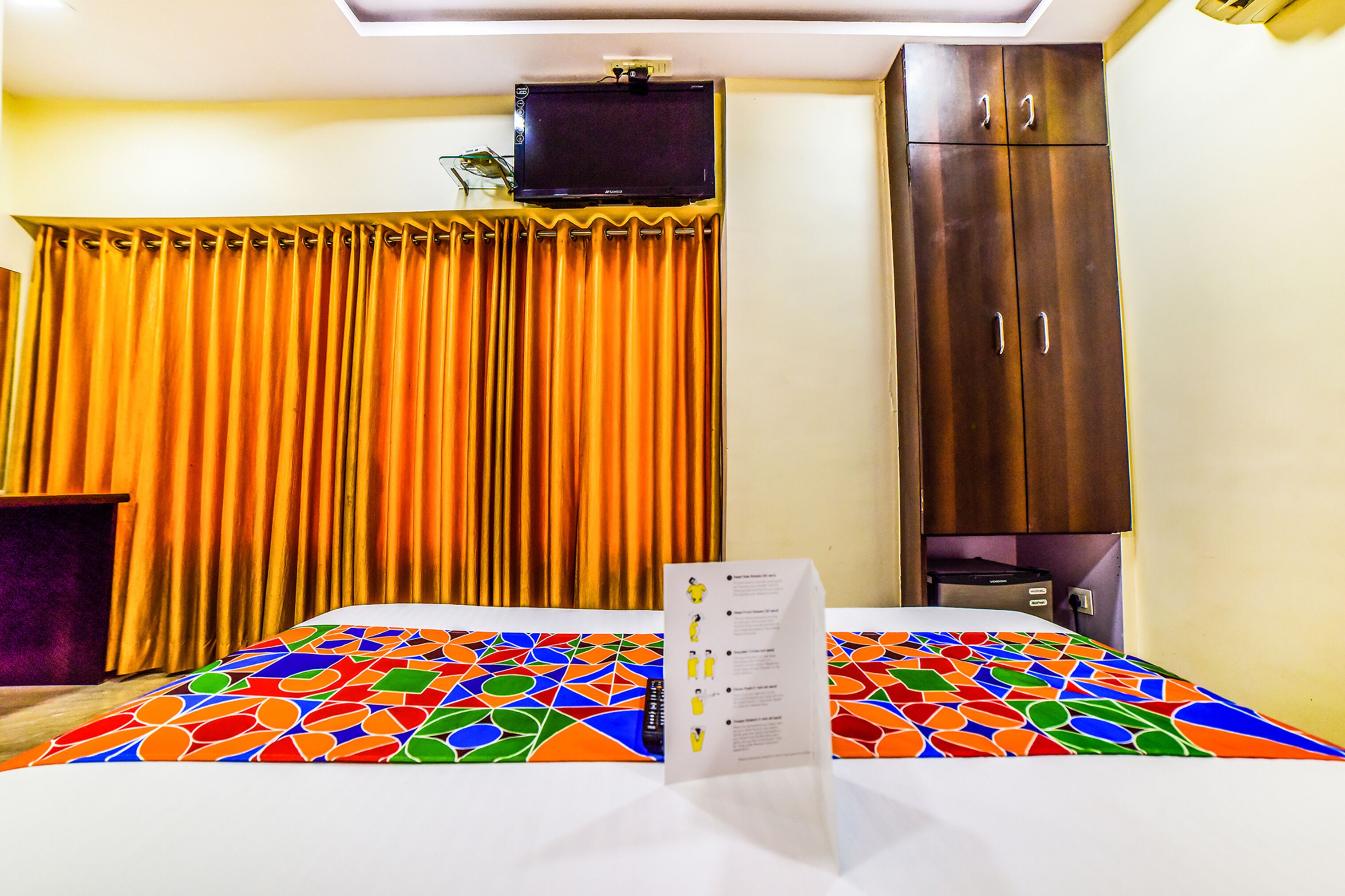 Una camera d'albergo con un letto, una televisione a parete, un armadio e una tenda.