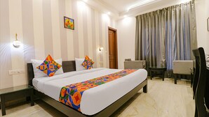A hotel room with a large bed, a desk, and a chair. There are two wall-mounted lamps and a door. - Fabhotel Rr Residency (Gurugram)