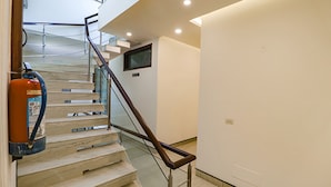 A staircase with wooden steps and metal railings, a fire extinguisher mounted on the wall, and a flat-screen TV mounted on the wall. - Fabhotel Rr Residency (Gurugram)