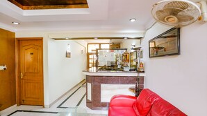 A hotel lobby with a red leather sofa, a reception desk, a wooden door, and a ceiling fan. - FabHotel Altus - DLF CyberHub, Gurugram (Gurugram)