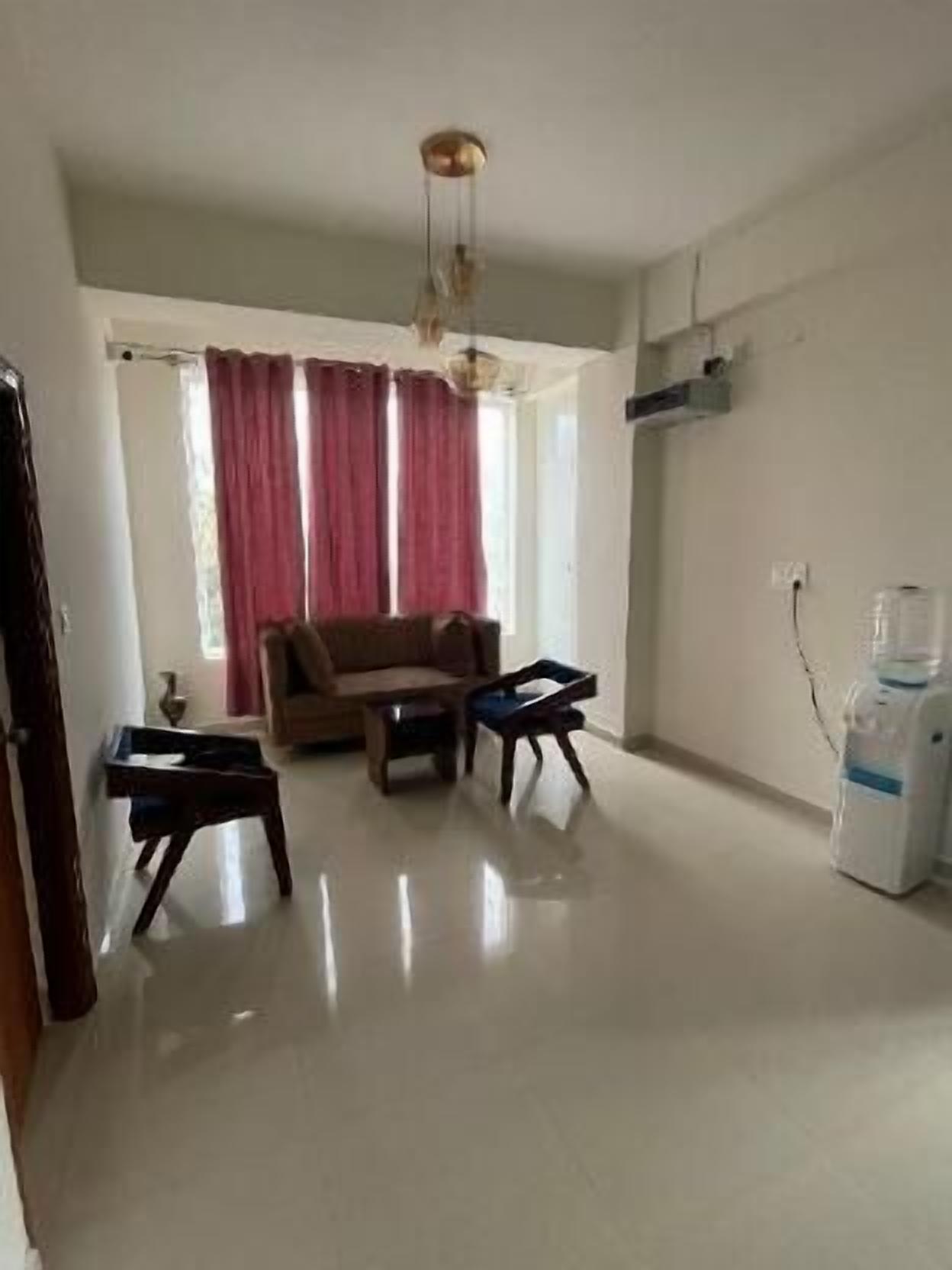 A living room with a sofa, two small tables, a water dispenser, and a window with curtains.
