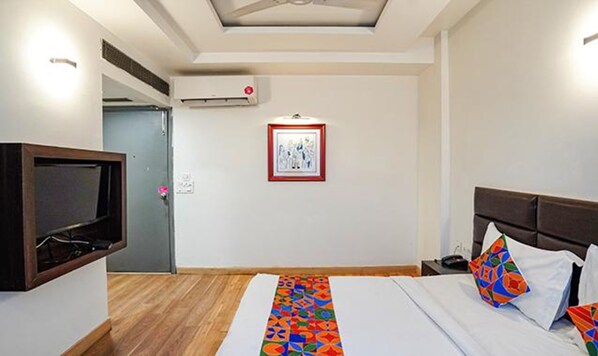 A hotel room with a bed, a TV, a framed picture on the wall, and an air conditioning unit.