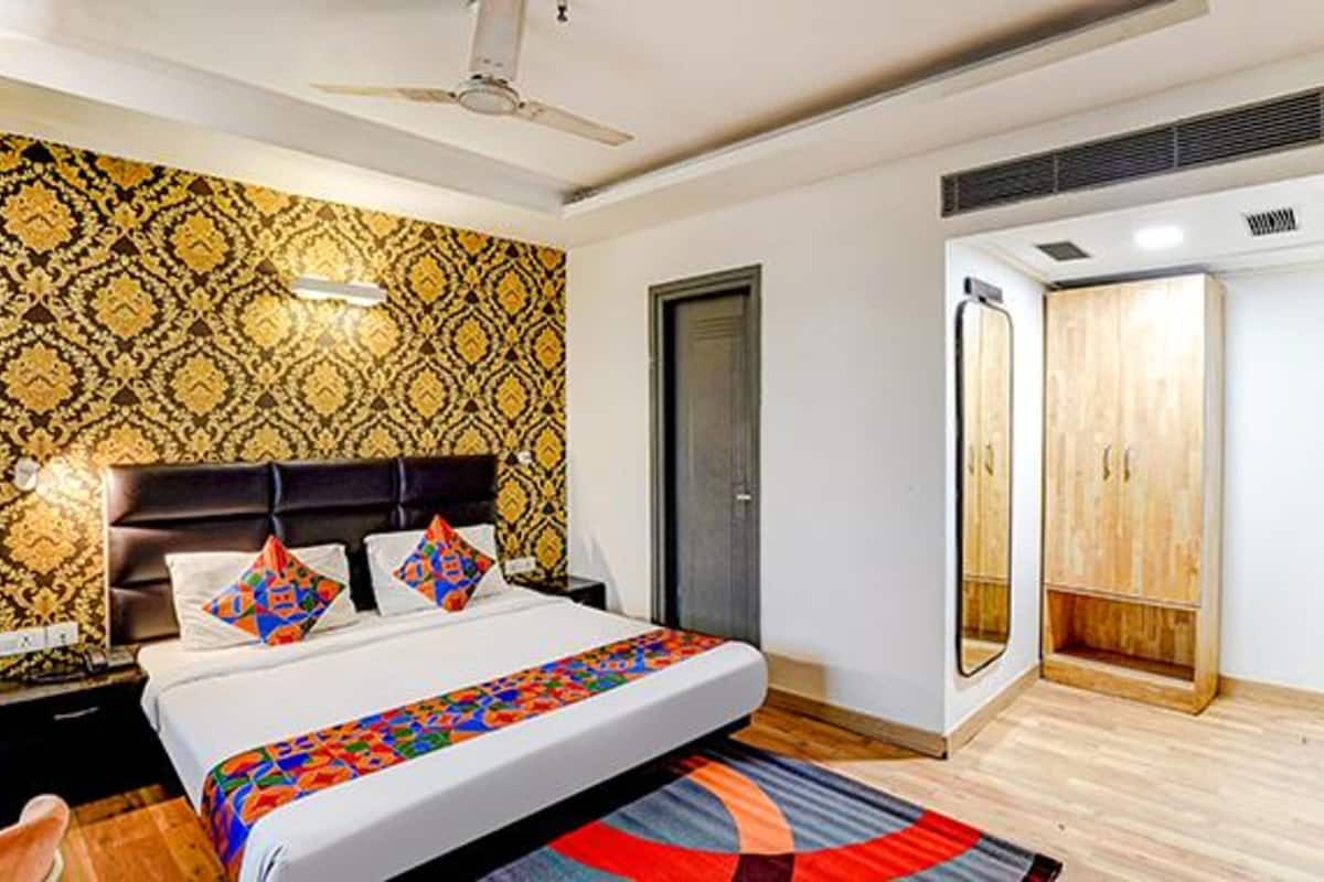 Quarto com papel de parede estampado, cama com roupa de cama colorida, guarda-roupa de madeira e ventoinha no teto.
