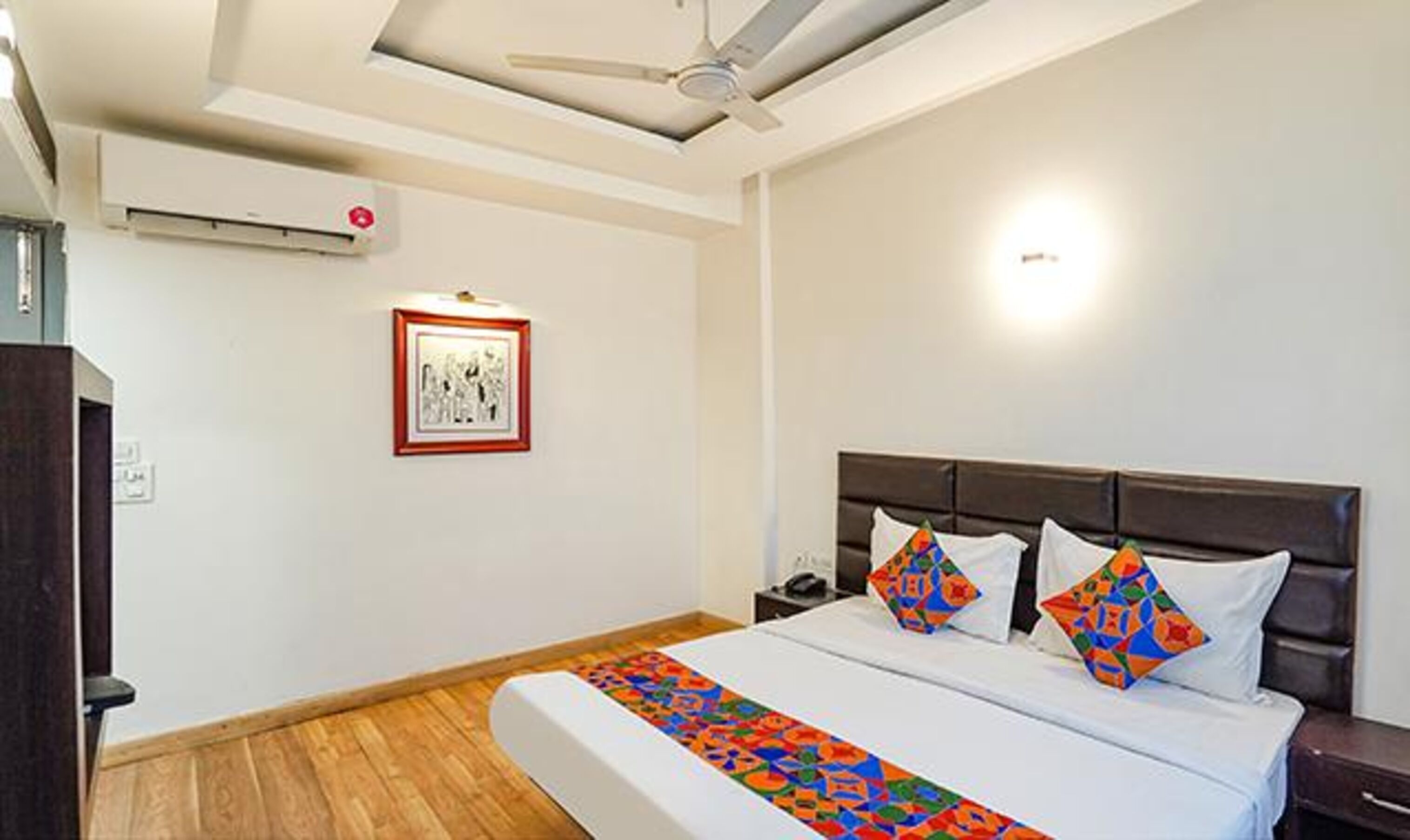 Une chambre d’hôtel avec un lit, un ventilateur de plafond, un tableau encadré au mur et une table de chevet.