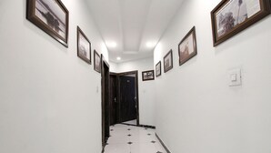Un couloir aux murs ornés de tableaux encadrés, doté d’un sol carrelé et terminé par une porte.