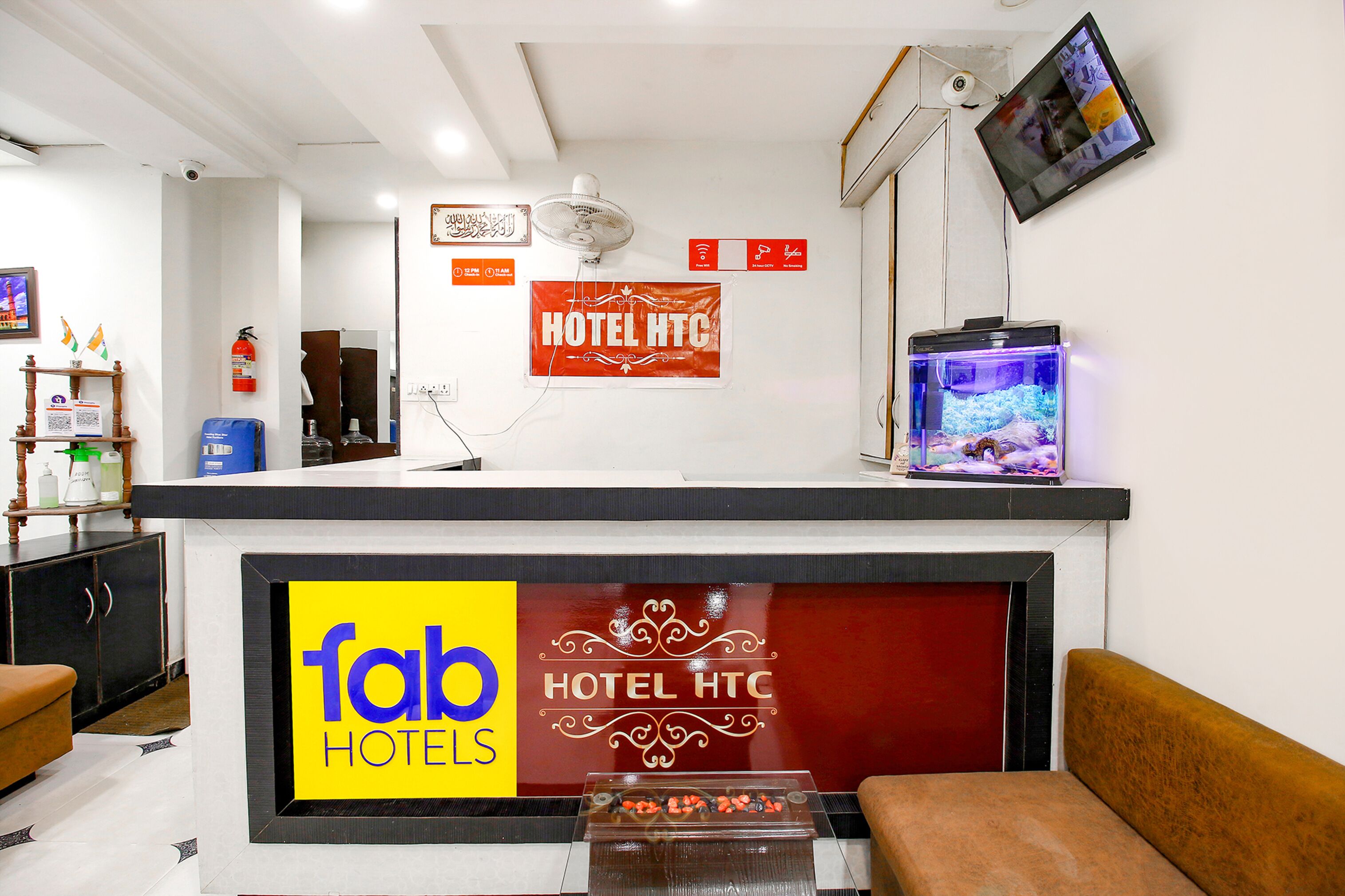 Un espace d’accueil d’hôtel comprenant un comptoir de réception, un aquarium, un extincteur et un téléviseur fixé au mur.