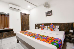 A hotel room with a large bed, a wooden headboard, a desk with a chair, an air conditioner, a wall-mounted fan, and a picture on the wall. - FabHotel HTC (Bhopal)