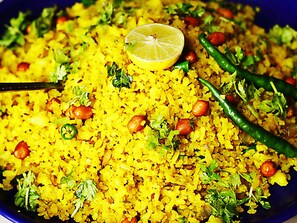 A plate of yellow rice with peanuts, green chilies, and a lemon slice. - FabHotel HTC (Bhopal)