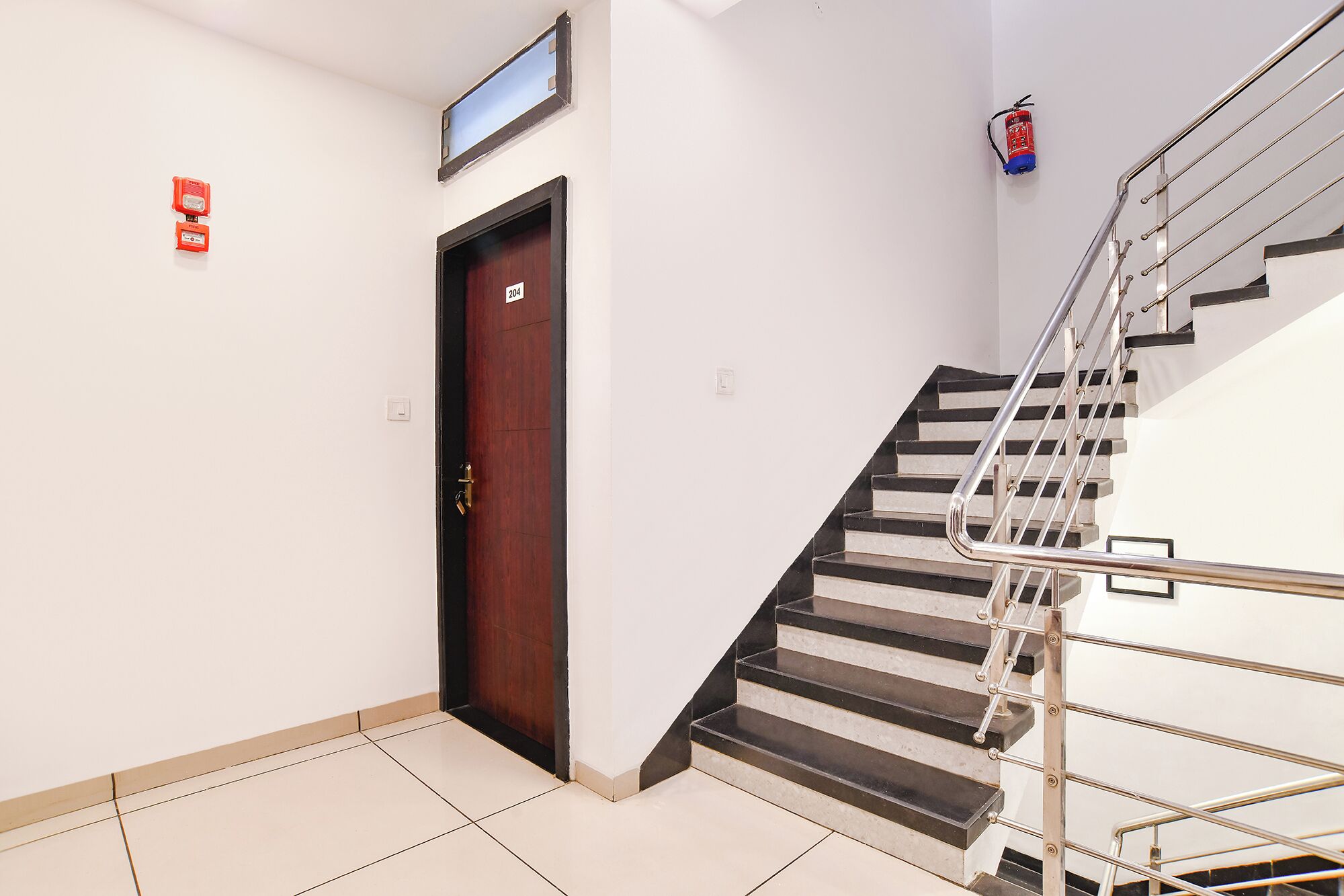 A staircase with metal railings, a wooden door with a number plate, and a fire extinguisher on the wall.