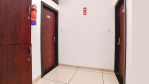 A hallway with two wooden doors, a fire alarm, and a light switch on the wall.