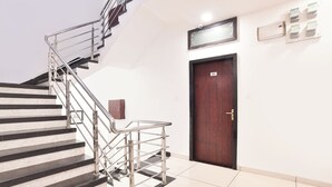 A staircase with metal railings, a wooden door with a number plate, and a small cabinet.