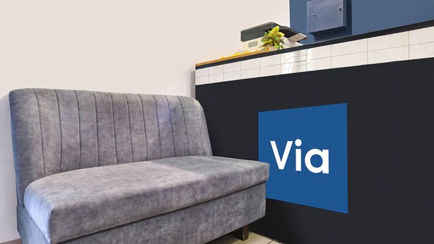 A grey sofa in a room with a blue wall and a 'Via' sign.