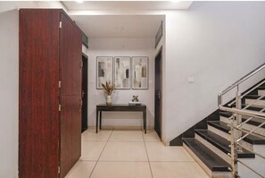 A hallway with a wooden wardrobe, a console table with decorative items, and a staircase with metal railings. - Via Sagar Sky (Indore)