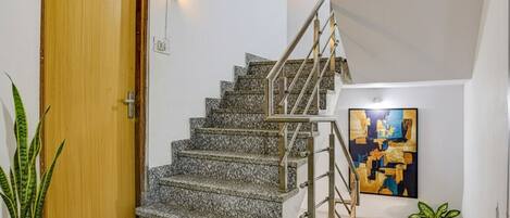 Un escalier avec des marches en granit et des rampes en métal, une porte en bois avec une plaque, et un tableau accroché au mur.