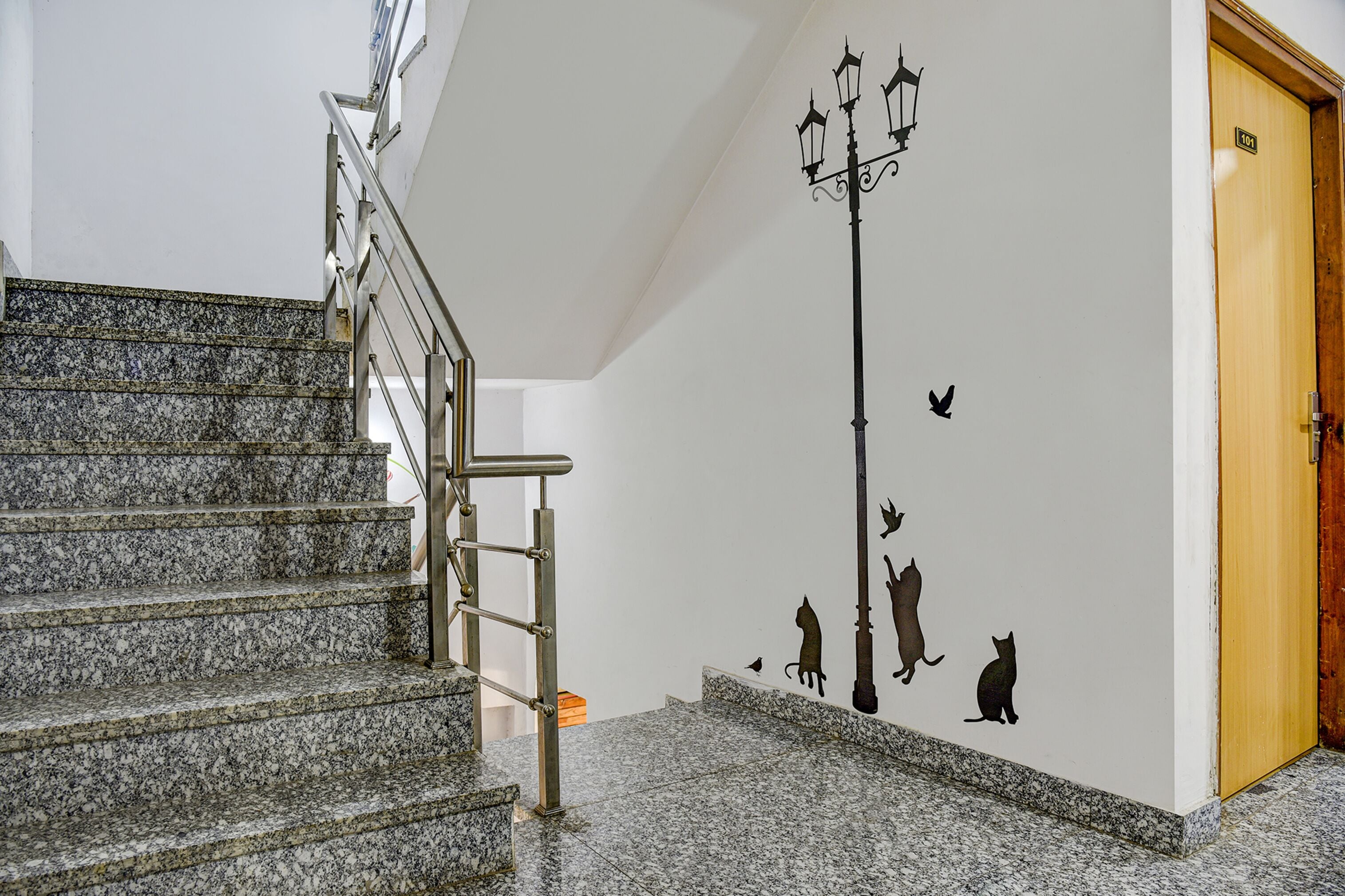 A staircase with a metal handrail, a wall with cat silhouettes, and a wooden door.