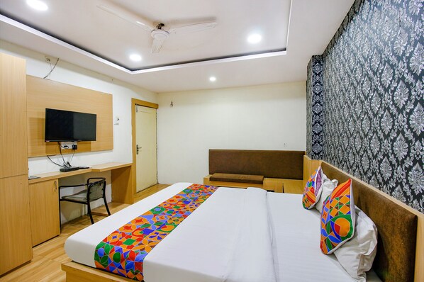 A hotel room with a bed, a desk, a chair, a television, and a patterned wall.