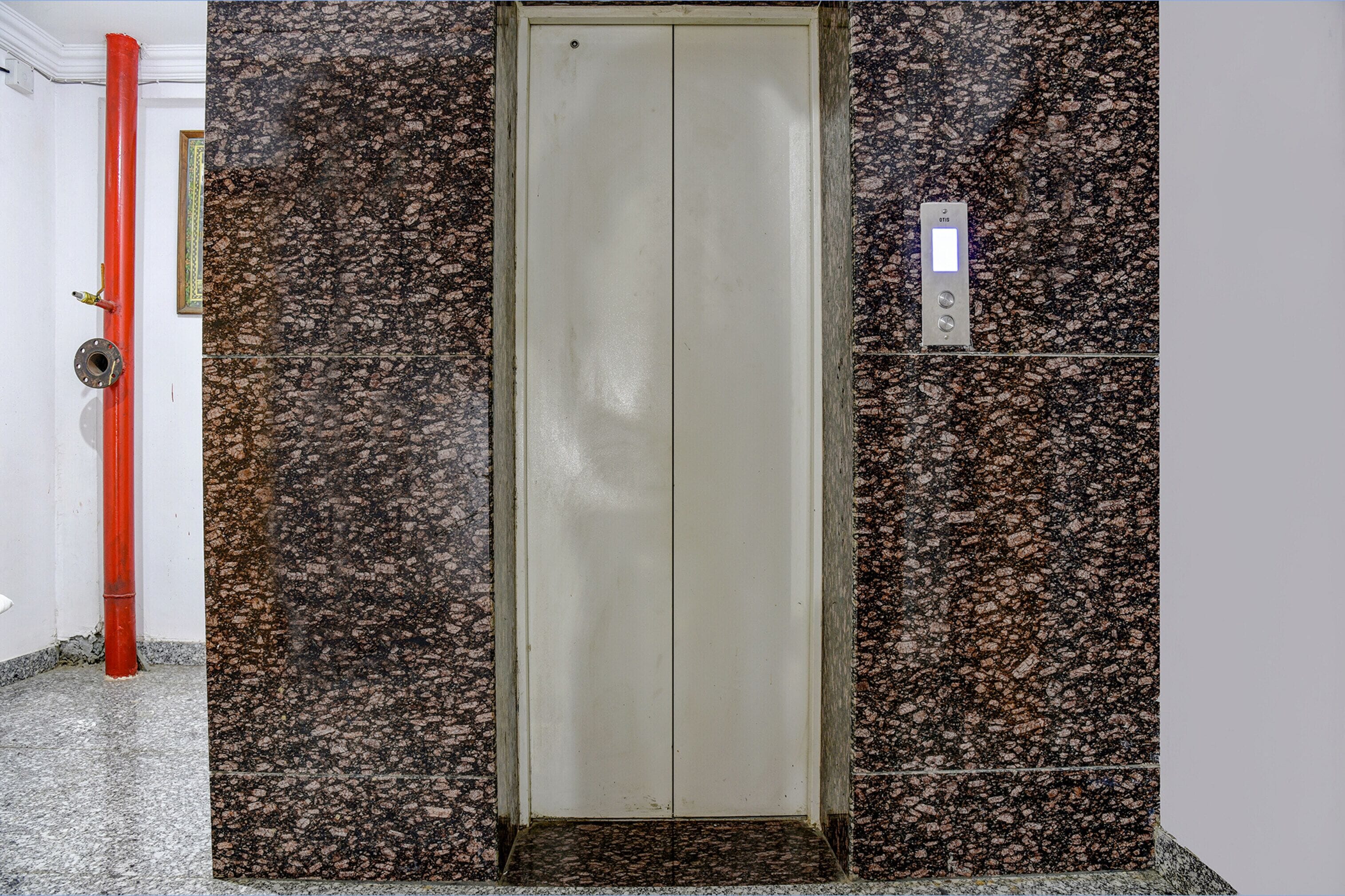 Un ascensor con pared de mármol, una tubería roja y un panel de control.