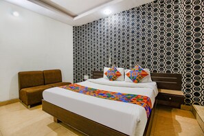 Un dormitorio con una cama, un sofá marrón, un papel tapiz estampado y una mesita de noche.
