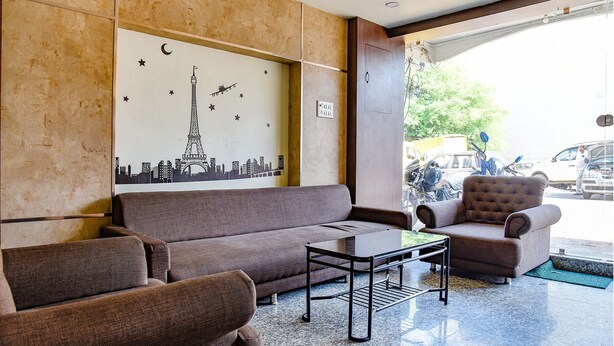 A lobby with a brown sofa, a small table, and a chair. There is a wall with a cityscape mural. - Fabhotel Surbhi (Bhopal)