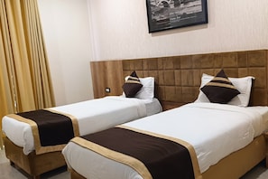 Habitación de hotel con dos camas individuales, cada una con cabecera marrón y ropa de cama blanca.