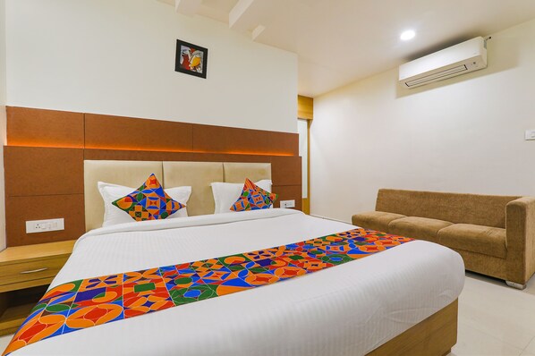 Une chambre d’hôtel avec un grand lit, un canapé marron, un plaid coloré et un climatiseur fixé au mur.